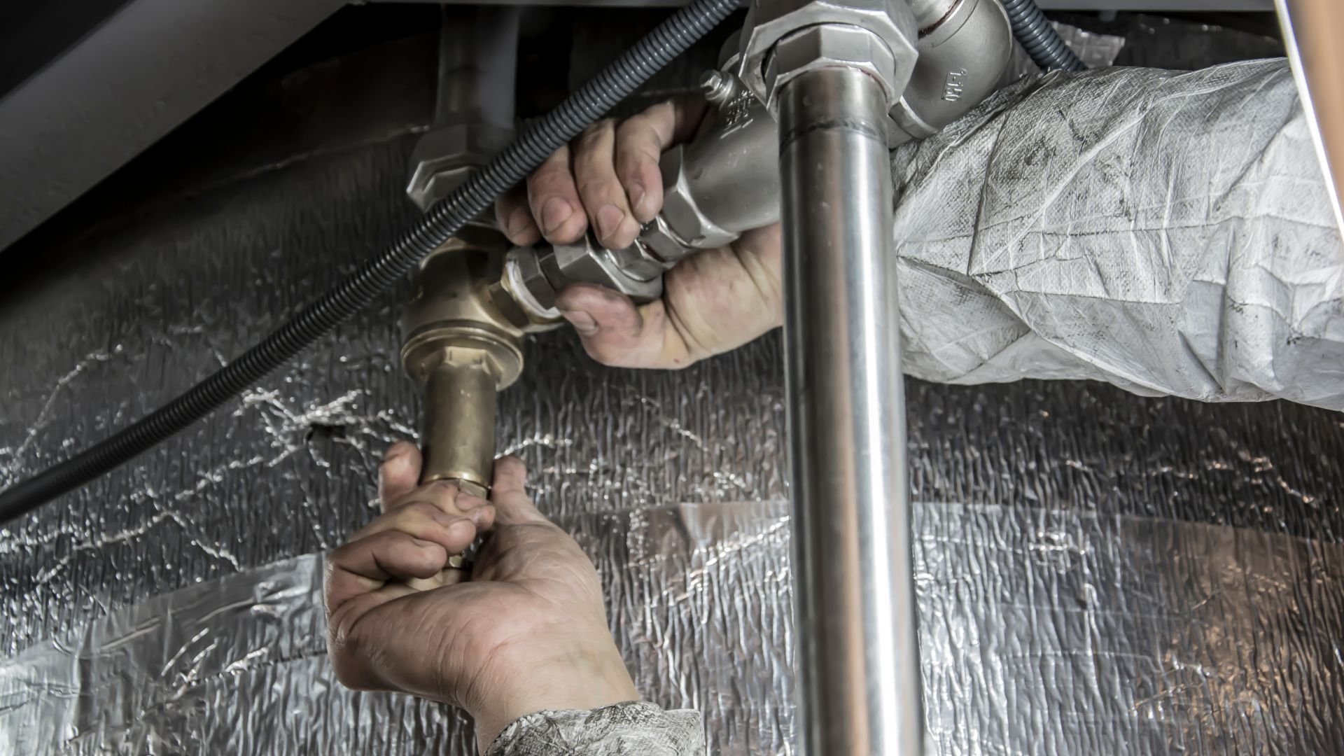Hands tightening plumbing pipe connection with metallic background